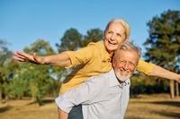 Das Bild zeigt einen älteren Mann, der eine ältere Frau auf dem Rücken trägt. 