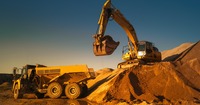 Das Bild zeigt einen Bagger, der auf einem Sandberg steht und Sand in einen LKW schaufelt. 
