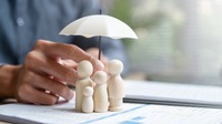 Holzfiguren symbolisieren eine Familie, geschützt durch einen Regenschirm