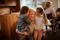 Das Bild zeigt einen Großvater, der von seinen Enkelkindern einen Kuss bekommt. 