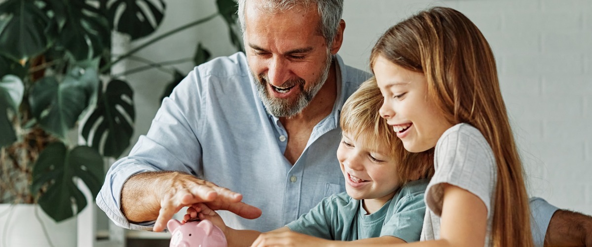 Großvater sitzt mit Enkeln vor einem Sparschwein